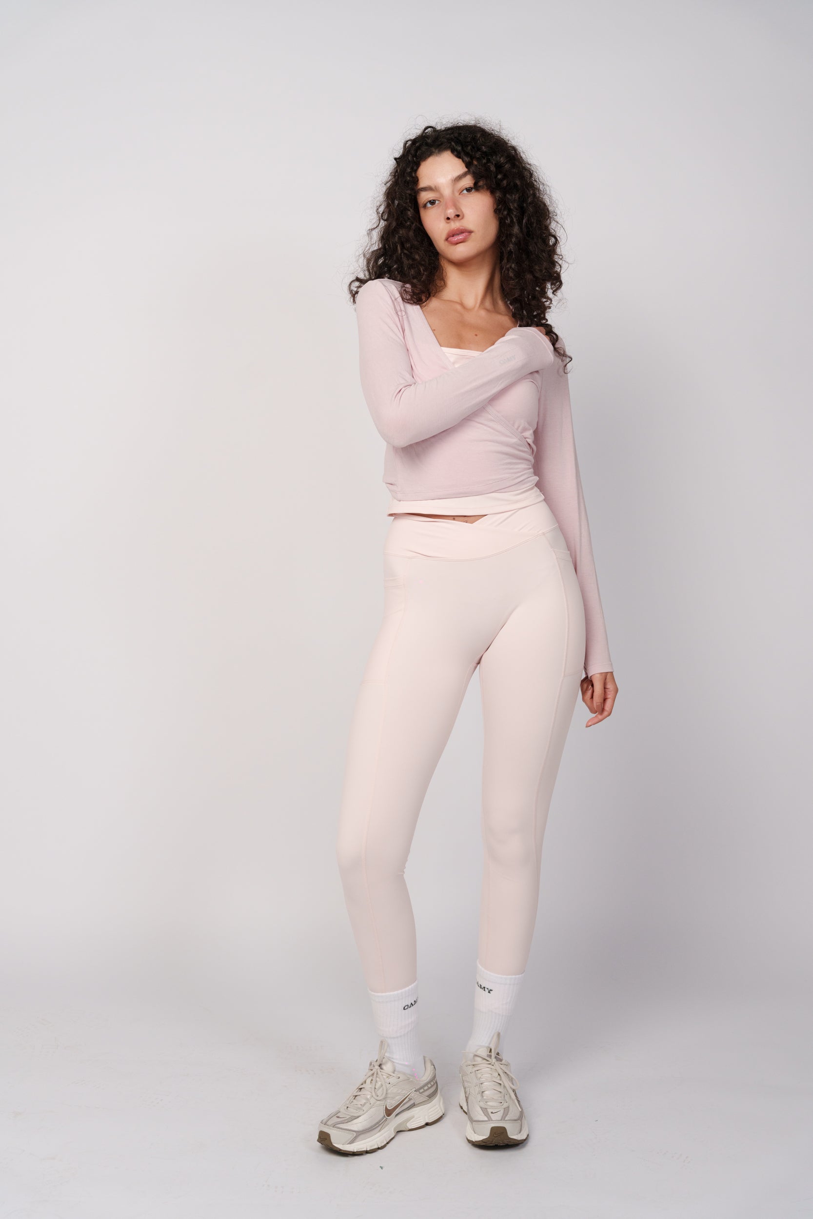 Woman wearing a light pink long-sleeve top and leggings on a white background