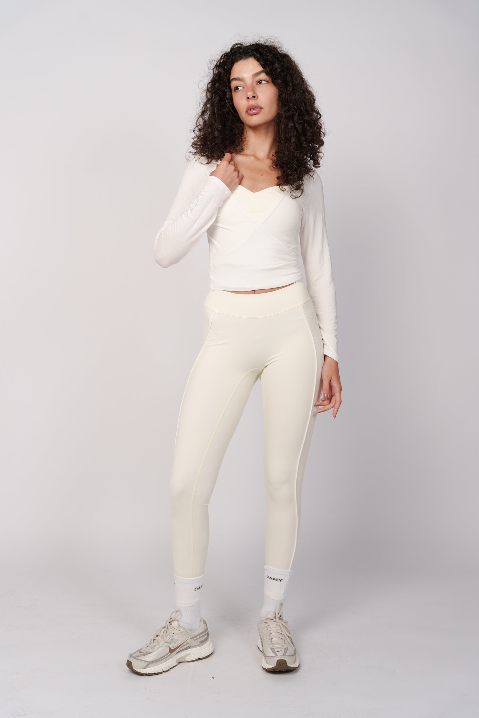 Woman wearing a white long-sleeve top and cream leggings on a light gray background