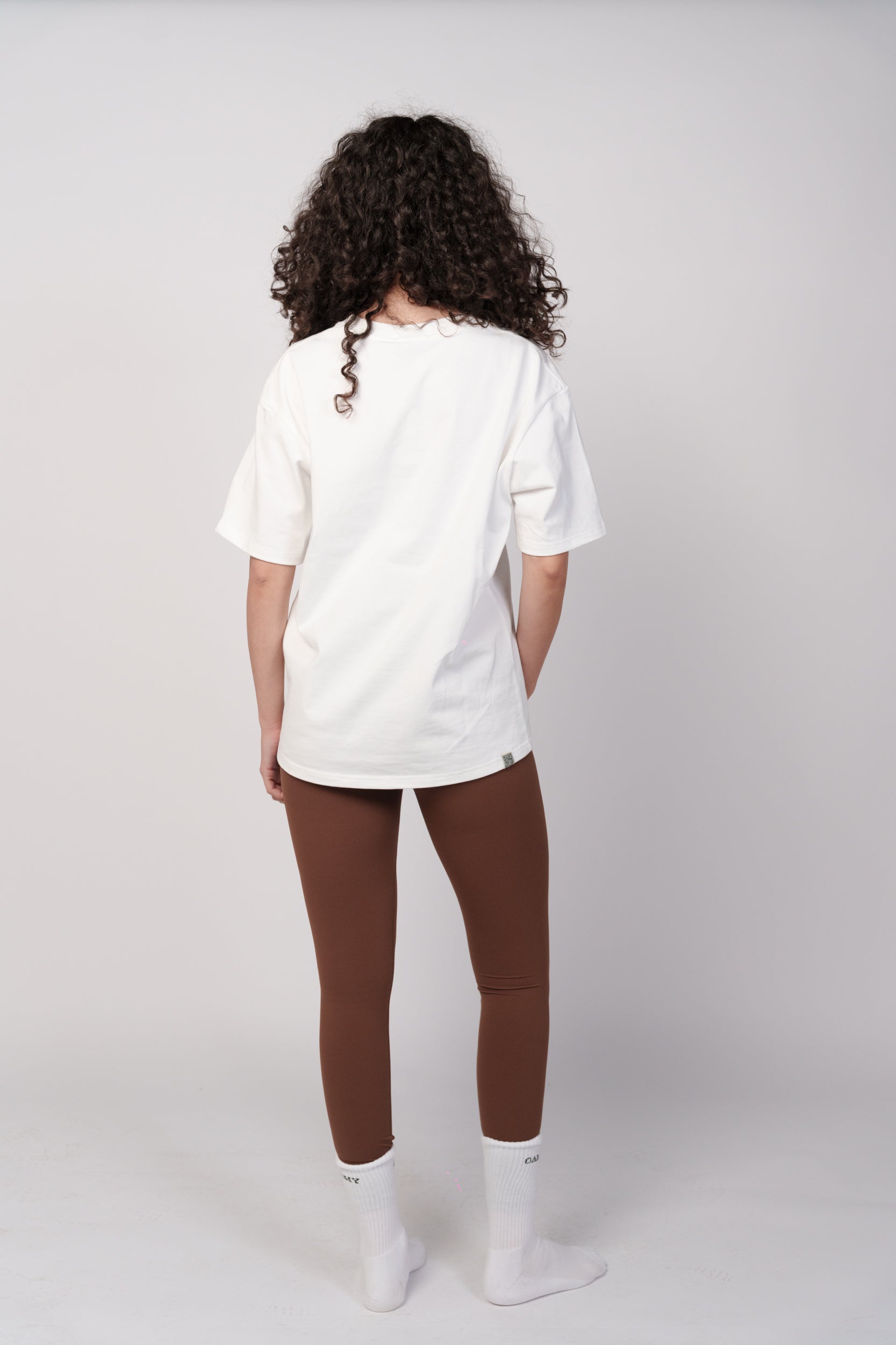 Person wearing a white oversized shirt and brown leggings on a plain background