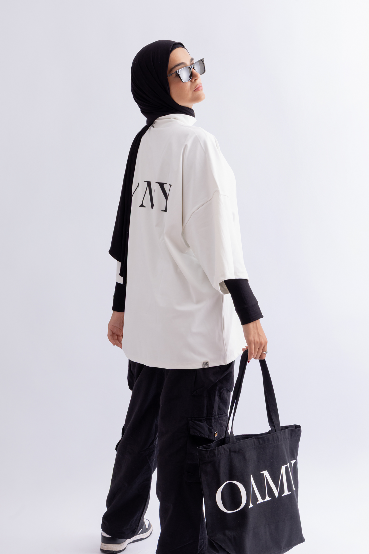 Model wearing the OAMY Super Oversized Soft Skin T-Shirt in White with black Cargos and a black headscarf, holding a black tote bag.