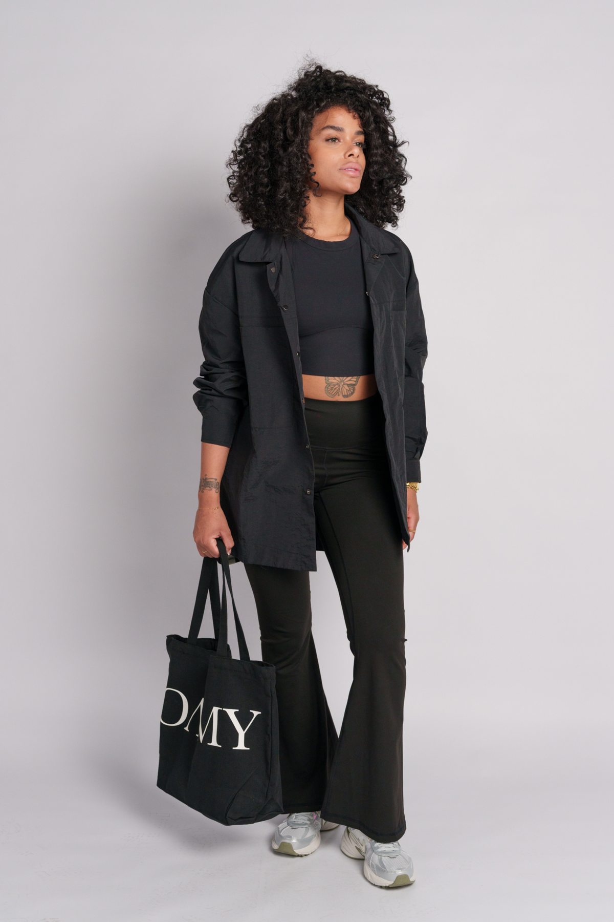 Model wearing a black shacket with a tote bag and a black flares.