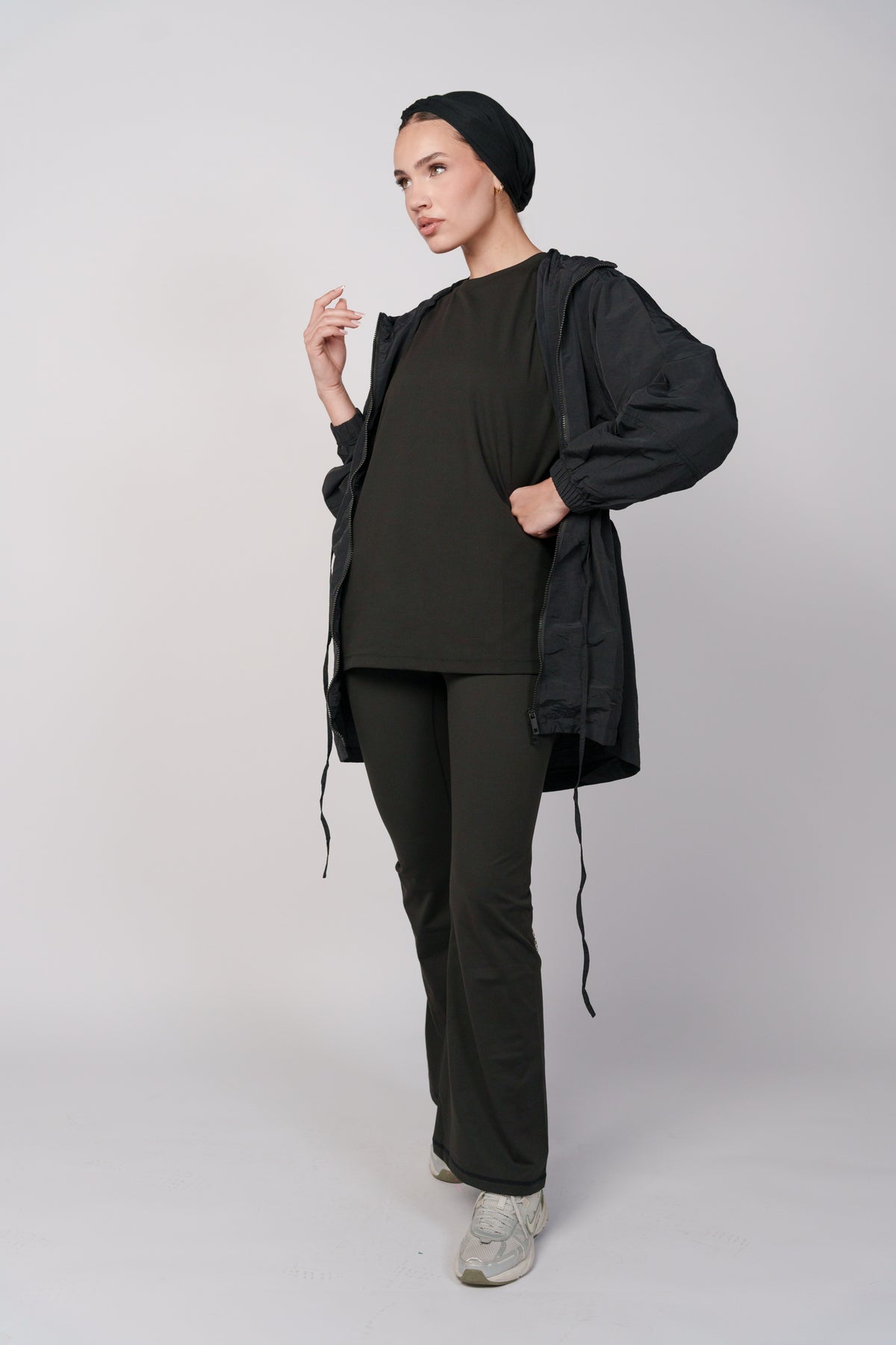 Woman wearing a black jacket with a hood , a black oversized t-shirt and a black flared pant.