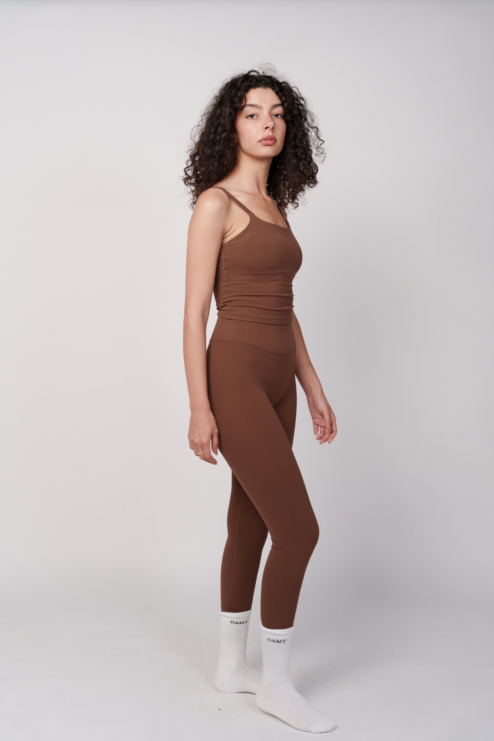 Woman wearing a brown sleeveless top and leggings set on a white background