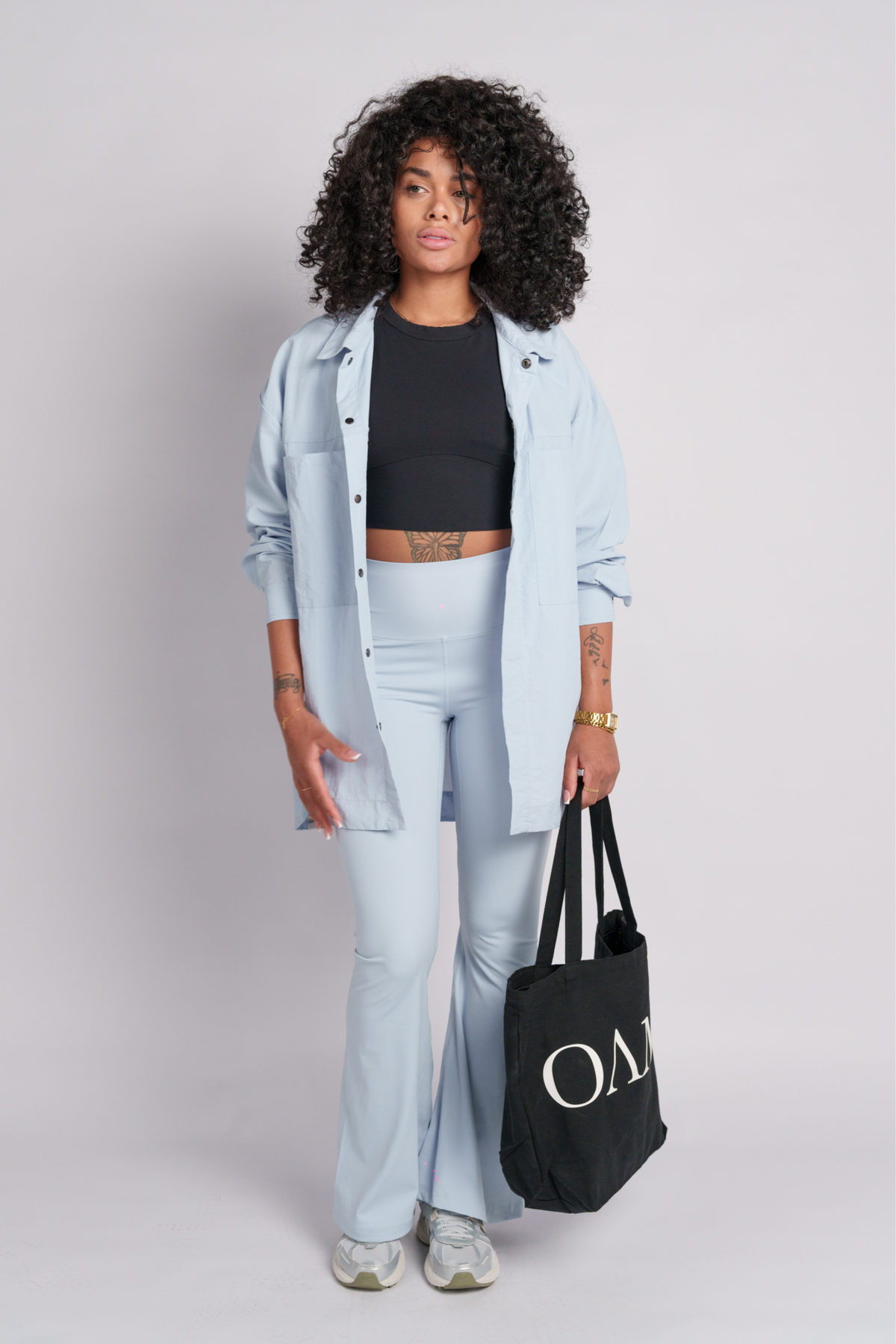 Woman wearing baby blue shirt and flare pants holding a black tote bag with  "OAMY" logo.