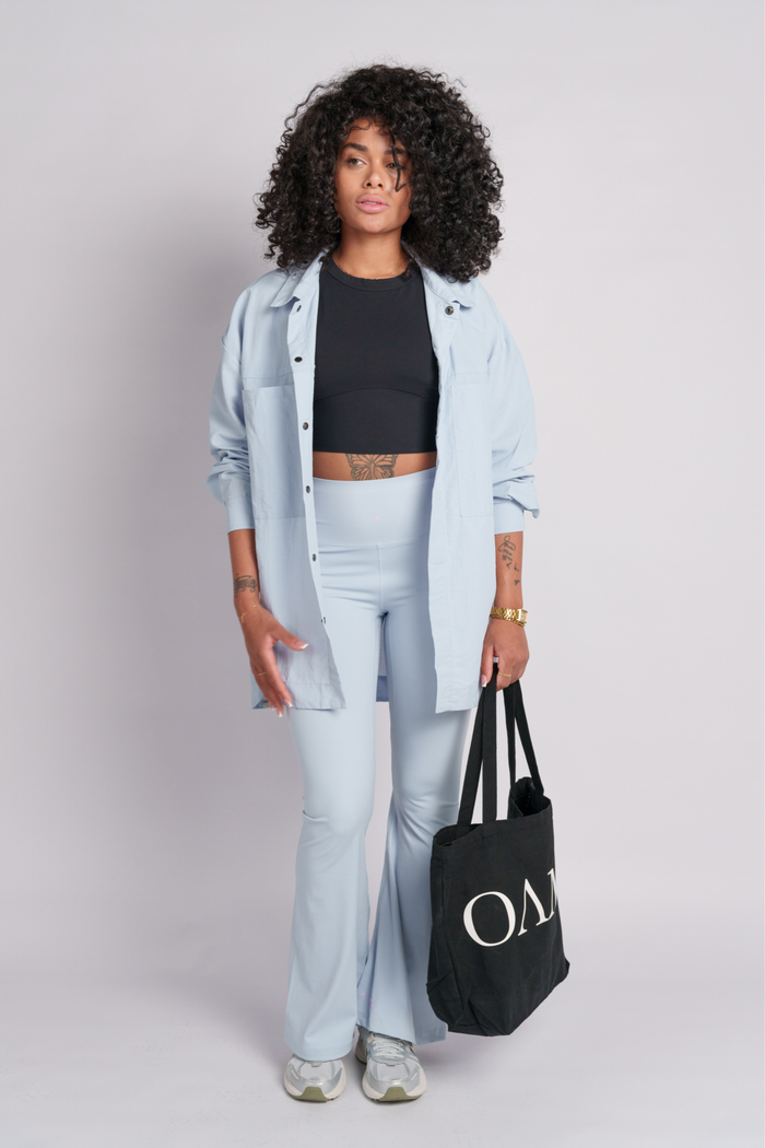 Woman wearing baby blue shirt and flare pants holding a black tote bag with  "OAMY" logo.
