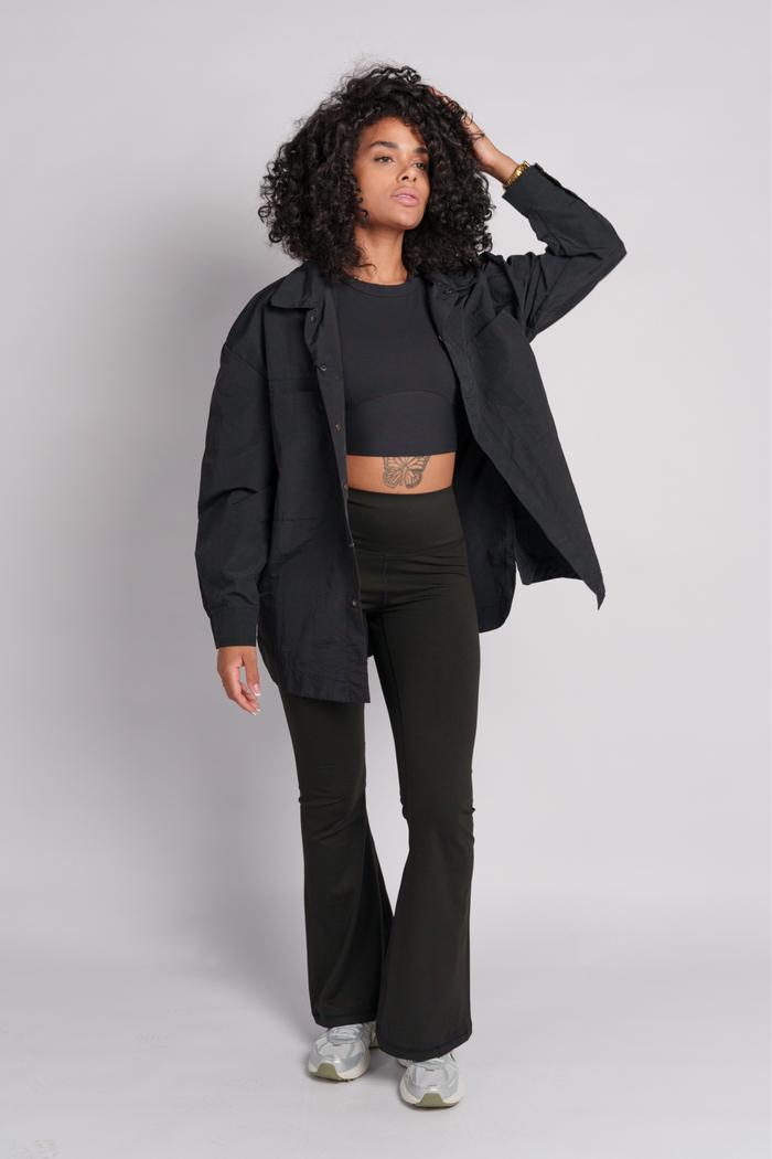 Woman wearing a black shacket with a black flare and a black crop top.